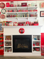 A red and white display shelf with a fireplace and many Coca Cola products and retro diner decor within the interior of Ice Dreams Soda Shop.