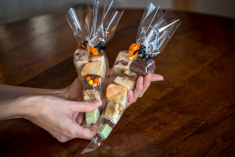 2 hands hold 2 packages of individually gift wrapped Lucky Duck Fudge portions in cellophane cones and tied with ribbons. 
