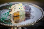 A small gift wrapped portion of Lucky Duck Fudge with 3 flavours in cellophane wrapping and tied with a green string and a gift tag reading "Thank you!" sitting on a silver mirror. 