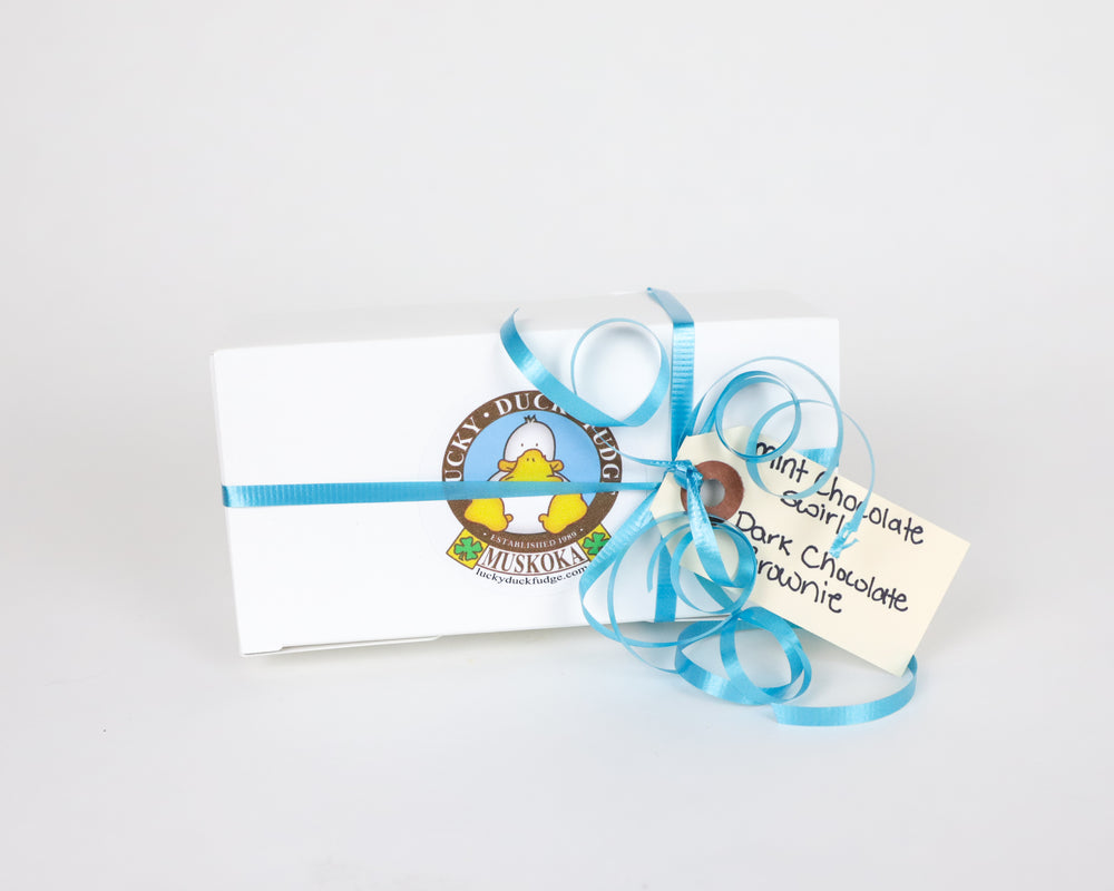 A small gift wrapped box of Lucky Duck Fudge decorated with a blue curled ribbon and a gift tag reading "Mint Chocolate Swirl" and "Dark Chocolate Brownie" set on a white background. 